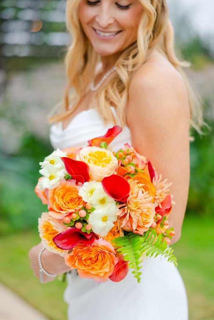 bride holding her bouquet with orange, red, pink, yellow, and white flowers 